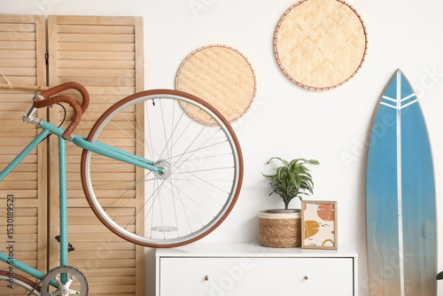 Interior of living room with chest of drawers, bicycle and surfboard near white wall