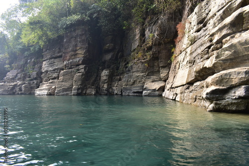 Emerald river water of Dawki flows between sheer rock cliffs, serene natural beauty.
