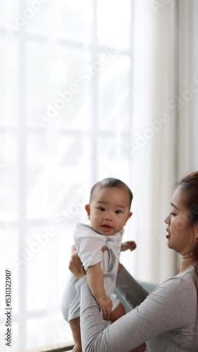 Happy mother lifting and playing with her baby at home, warm maternal bond and joyful family in home.