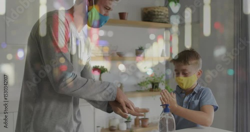 Father picking up sanitizer pump at kitchen counter and guiding son rubbing gel for health safety