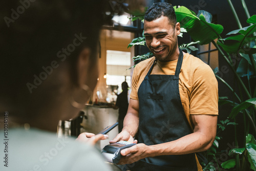 Canvas Print Happy waiter accepting contactless payment from customer in cafe