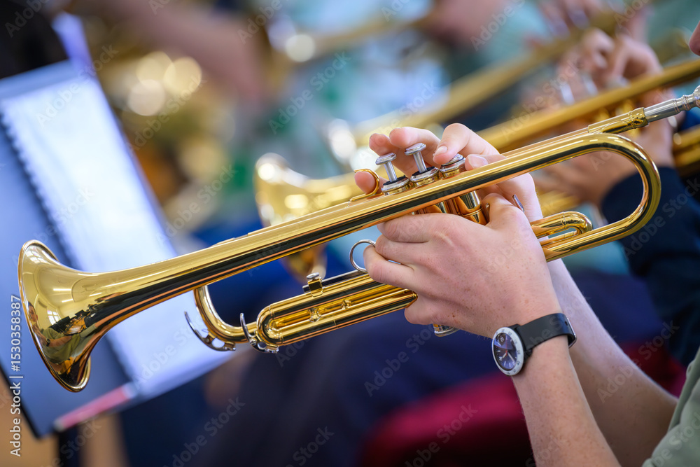 Obraz premium A trumpet being played by a youth in the foreground with other trumpets blurred in the background.