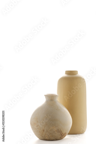 Vertical image of two modern minimalist vases in soft sand tones, backlit with bright white light. The elegant simplicity and neutral palette