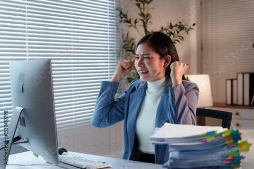 Photos Asian businesswoman covering ears with hands and clenching teeth while working o