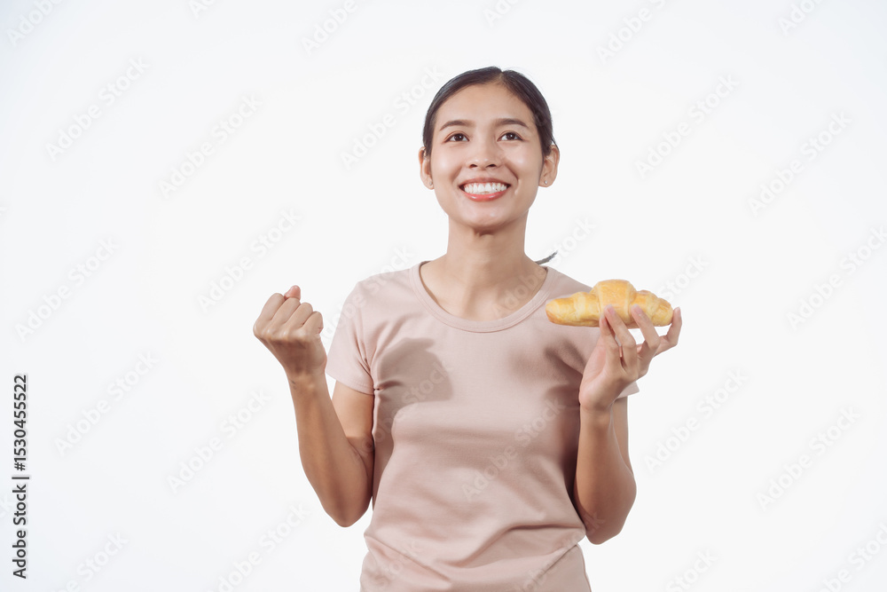 A confident young Asian woman in a light brown shirt stands against a white background, happily holding a delicious croissant in her hand, ready to enjoy a fresh and tasty pastry snack. A confident young Asian woman in a light brown shirt stands against a white background, happily holding a delicious croissant in her hand, ready to enjoy a fresh and tasty pastry snack.