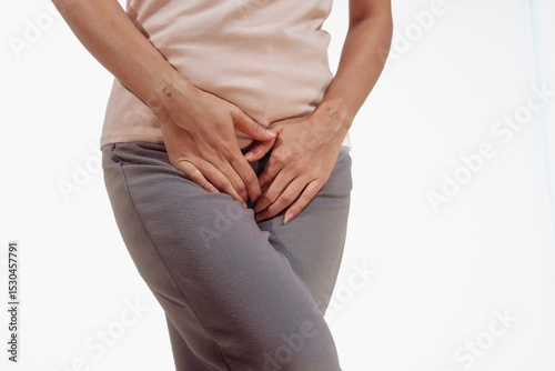 Papier peint Confident young Asian woman in light brown shirt stands against a white background, experiencing vaginal pain