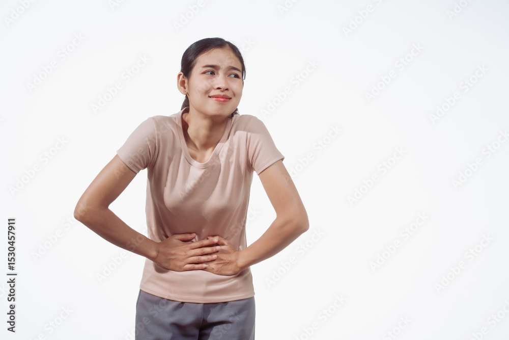 Fototapeta premium A confident young Asian woman in a light brown shirt stands against a white background, experiencing abdominal pain. Causes may include menstrual cramps, ovarian cysts, endometriosis
