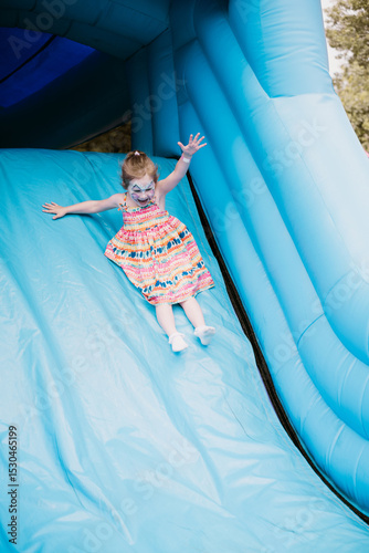 Toddler girl sliding on a bouncy castle, summer holiday