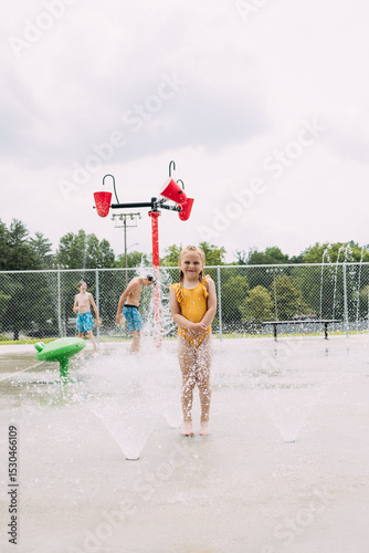 Smiling child standing in sprinklers while kids play in splash pad