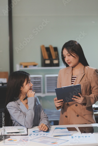 Two young Asian business woman talk, consult, discuss working with new startup project idea presentation analyze plan marketing and investment in the office.
