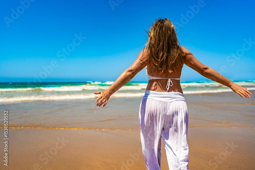 Happy middle aged woman walking on sandy beach in summertime. Back view	