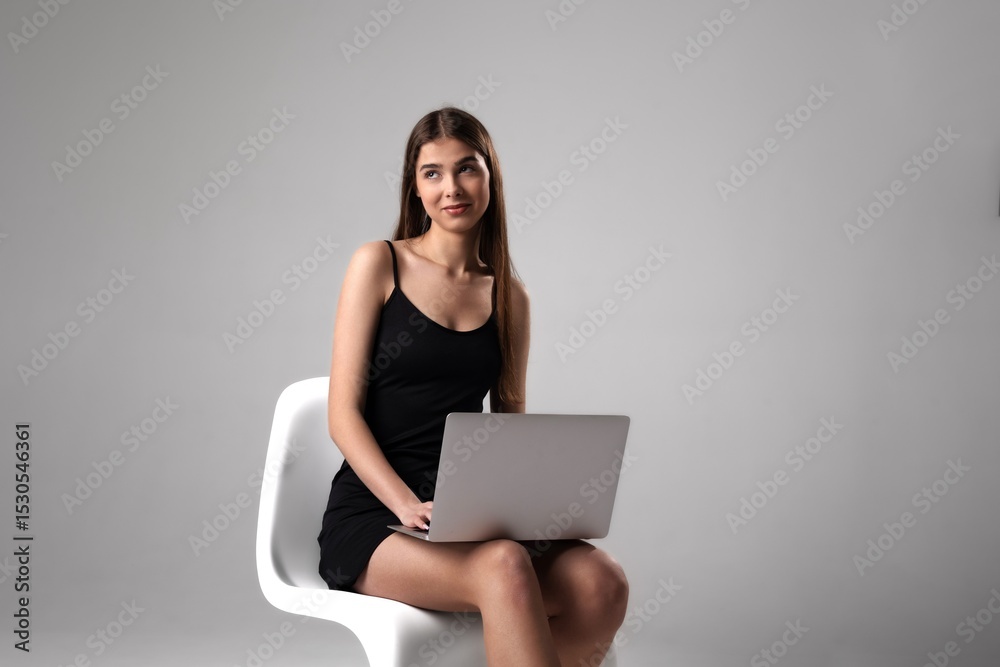 Young woman working on laptop while seated in modern chair during indoor session Young woman working on laptop while seated in modern chair during indoor session