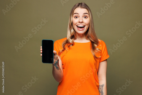 Young shocked surprised woman she wears orange t-shirt casual clothes hold in hand use mobile cell phone with blank screen workspace area isolated on plain pastel green background. Lifestyle concept.