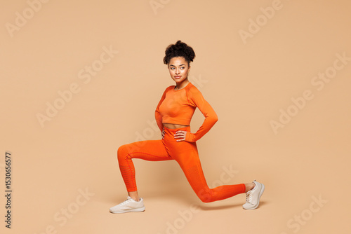 Full body young fitness trainer instructor sporty woman sportsman wear orange clothes spend time in gym do squat lunges stretch legs isolated on plain beige background. Workout sport fit abs concept.
