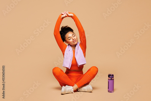 Full body young fitness trainer instructor sporty woman sportsman she wear orange clothes towel spend time in gym sit raise up hands isolated on plain beige background. Workout sport fit abs concept.