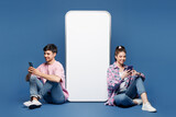 Full body young happy couple two friends family man woman wear pink casual clothes together sit near big huge blank screen mobile cell phone with area use smartphone isolated on plain blue background.