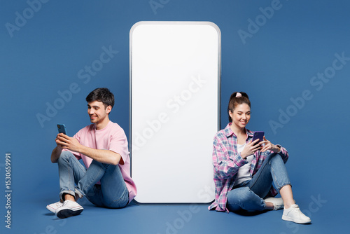 Full body young happy couple two friends family man woman wear pink casual clothes together sit near big huge blank screen mobile cell phone with area use smartphone isolated on plain blue background.