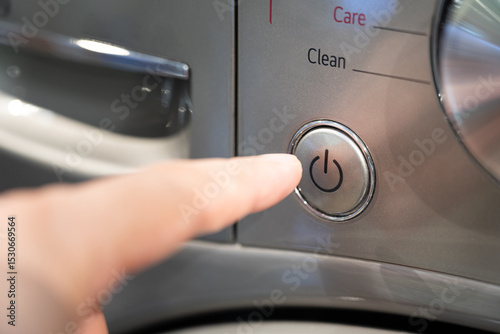 Finger Pressing Power Button on Modern Appliance. Pressing the start button on a washing machine. Close up view of automatic washing machine. photo