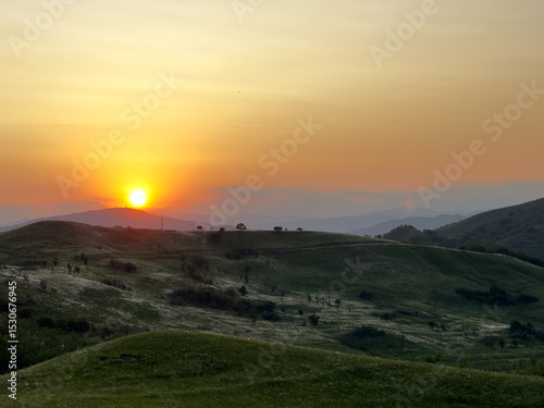 Buzău Green Hills Sunset. 
A serene landscape view captures rolling green hills in Buzău County, Romania, bathed in the warm hues of a sunset. 
