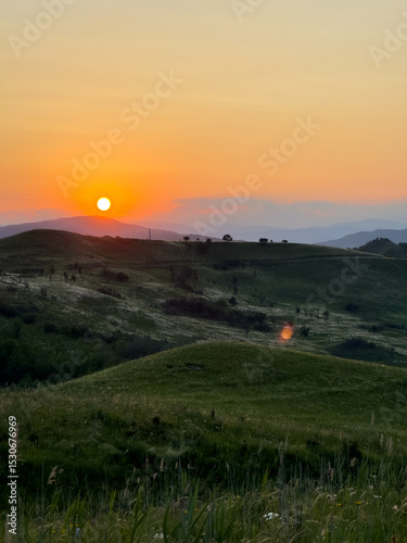 Buzău Green Hills Sunset. 
A serene landscape view captures rolling green hills in Buzău County, Romania, bathed in the warm hues of a sunset. 