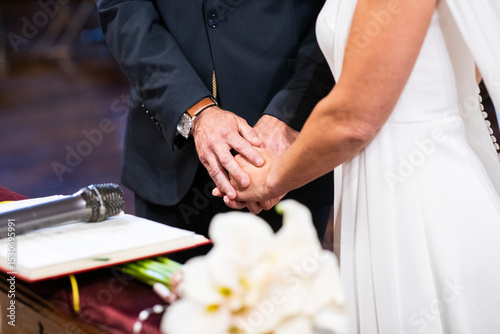 Una pareja casándose en una ceremonia religiosa, uniendo las manos, en el momento de la boda