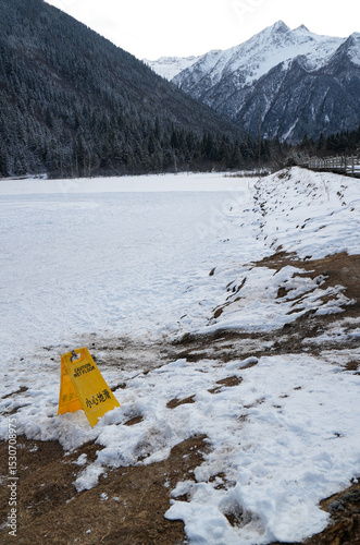 A frozen lake and field with snow-capped mountain landscape with caution sign yellow 