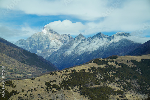 Mount Siguniang (Four Sisters Mountain) in Sichuan, China. The prominent snow-covered peak, The foreground features brown hills contrasting with alpine backdrop and a wide, vivid blue sky 