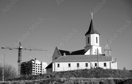 Old church with modern construction in background at daytime in urban setting.