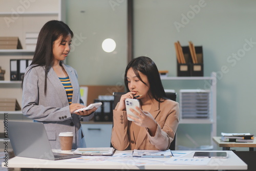 Two young Asian business woman talk, consult, discuss working with new startup project idea presentation analyze plan marketing and investment in the office.