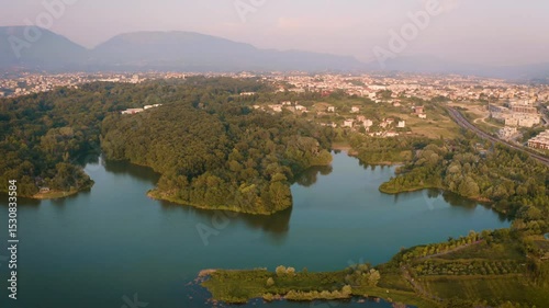 Forward drone shot over Tirana’s Grand Park, slowly veering left to reveal the skyline with its modern skyscrapers rising behind the dense forest, framed by a soft golden evening light.