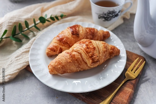 Two croissant in white plate with hot tea for morning breakfast or afternoon tea time
