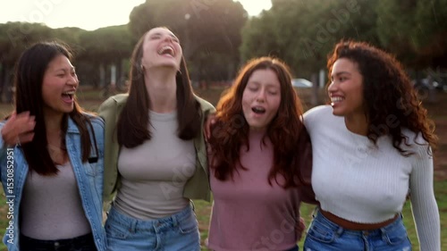 Multicultural group of young women walking together through sunlit park, sharing laughter, enjoying close friendship and genuine connection while bonding outdoors