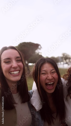 Four cheerful female friends are enjoying a sunny day at the park, laughing and embracing each other, creating a heartwarming scene of friendship and joy