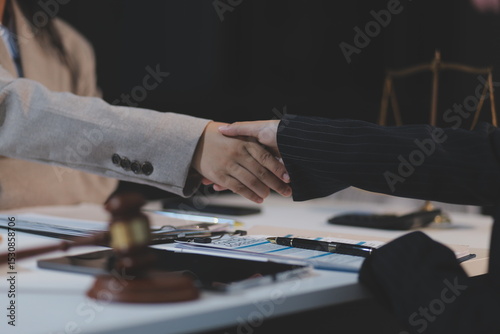 Lawyer shaking hands with a client making about documents, contracts, agreements, cooperation agreements with a female client at the lawyer's desk and a hammer at the table.