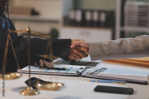 Lawyer shaking hands with a client making about documents, contracts, agreements, cooperation agreements with a female client at the lawyer's desk and a hammer at the table.