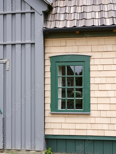 The old section of the vintage building has a grey exterior, while the newer addition sports light beige cedar shakes. The structure also includes a green wooden window with multiple glass panes