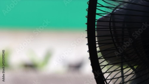 Detailed side view of an electric fan with focus on its metallic grille against a soft background