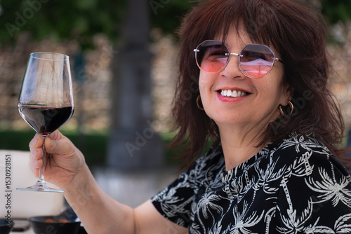Happy mature woman holding a glass of red wine, enjoying a moment of relaxation outdoors