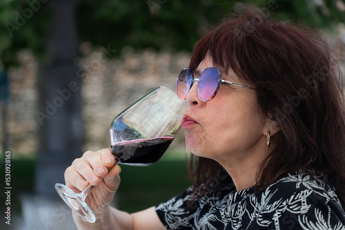 Senior woman wearing sunglasses savoring a glass of red wine in an outdoor setting