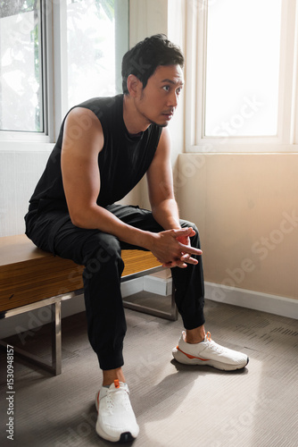 Asian man resting on bench in gym near sunlight window