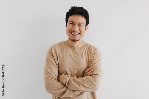 Smiling Asian man in beige shirt crossing arms confidently