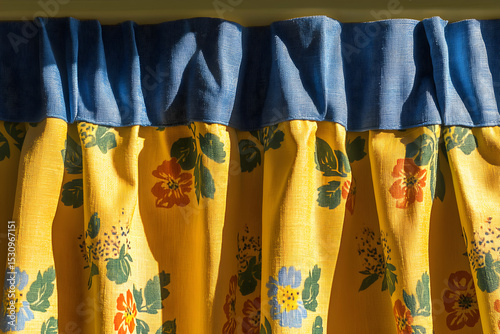 Close-up of yellow floral curtains with a blue top border, bathed in sunlight, showcasing texture and pattern details.