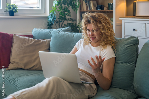 Young woman working from home on laptop experiencing technical issues such as internet disconnection, computer glitch or system error, frustrated and concerned while seated indoors