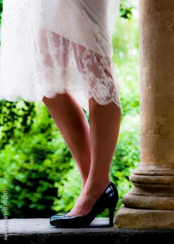 A woman in a white dress and black heels stands near a stone pillar.