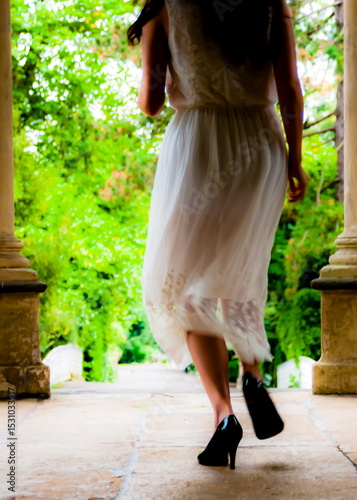 A woman in a white dress and black heels is walking away from the camera.