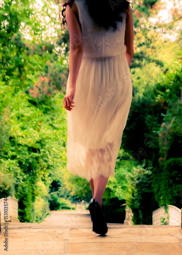 A woman in a white dress walks away from the camera on a stone path.