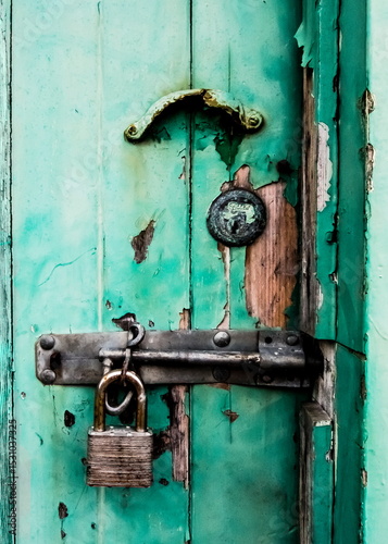 Close-up of a weathered, locked door with peeling paint and a rusty padlock.