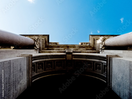 An upward view of an archway with columns and inscriptions, under a blue sky.