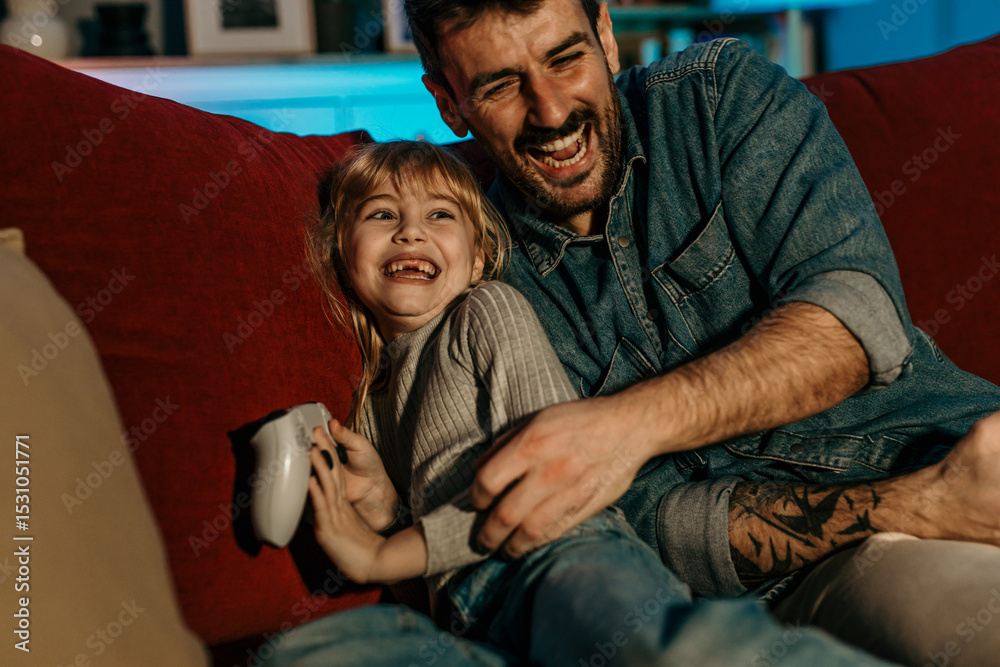Obraz premium Father and daughter laughing and playing video games on sofa at home