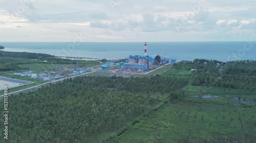 Aerial View of an Industrial Power Plant Surrounded by Lush Green Palm Trees Along the Seaside